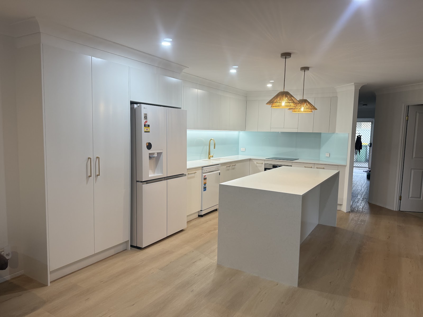 White kitchen with a white island bench, tall pantry cupboards and woven pendant lights