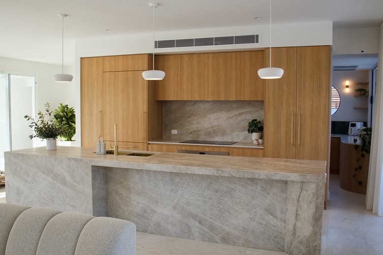 Wall of timber cabinetry with a stone waterfall island bench