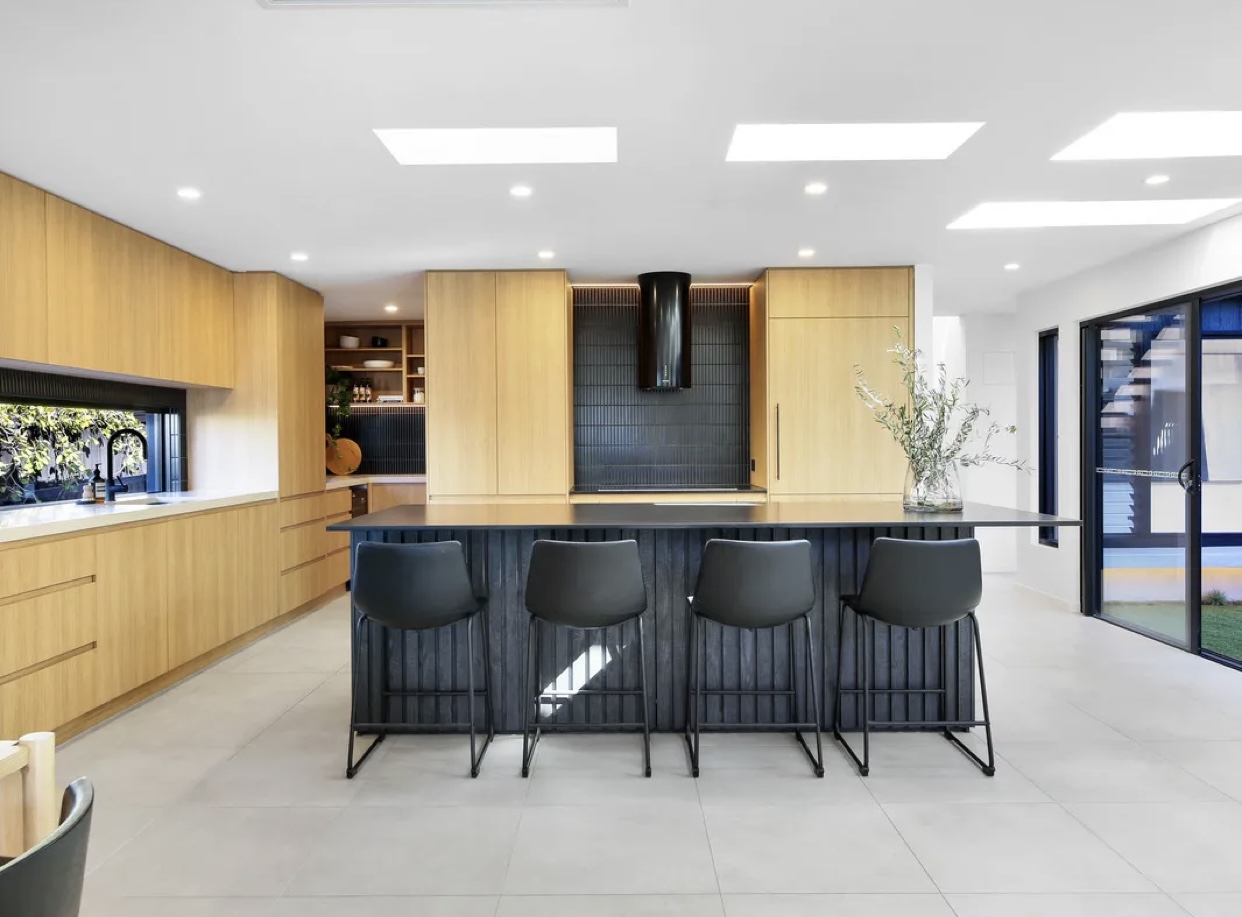Light oak kitchen with a black fluted island bench, black rangehood and four bar stools