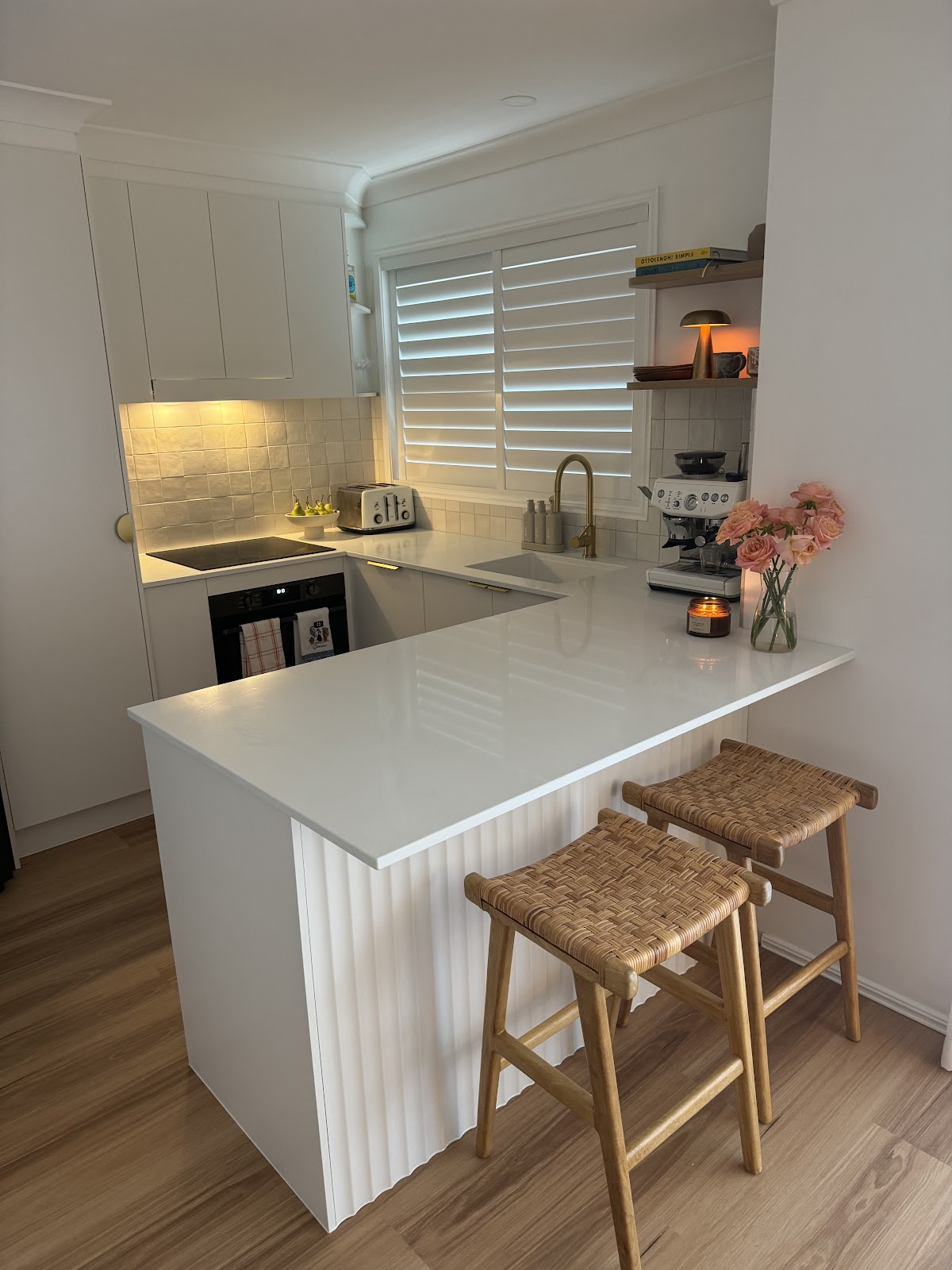 White townhouse kitchen with a fluted peninsula bench and rattan bar stools